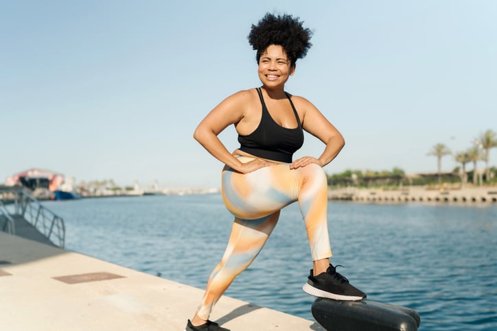 Plus size Hispanic woman in sportswear stretching legs before sport workout at the dock